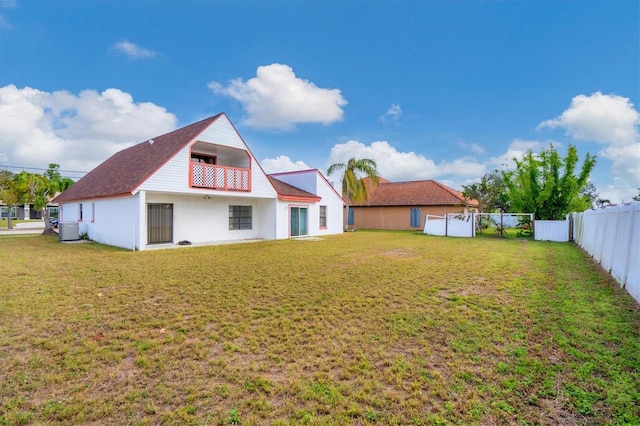 back of property with central AC unit, a lawn, and a balcony