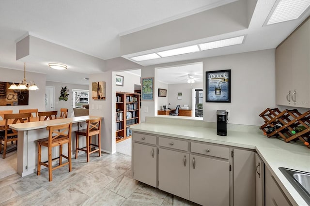 kitchen with gray cabinetry, ceiling fan with notable chandelier, kitchen peninsula, and a breakfast bar