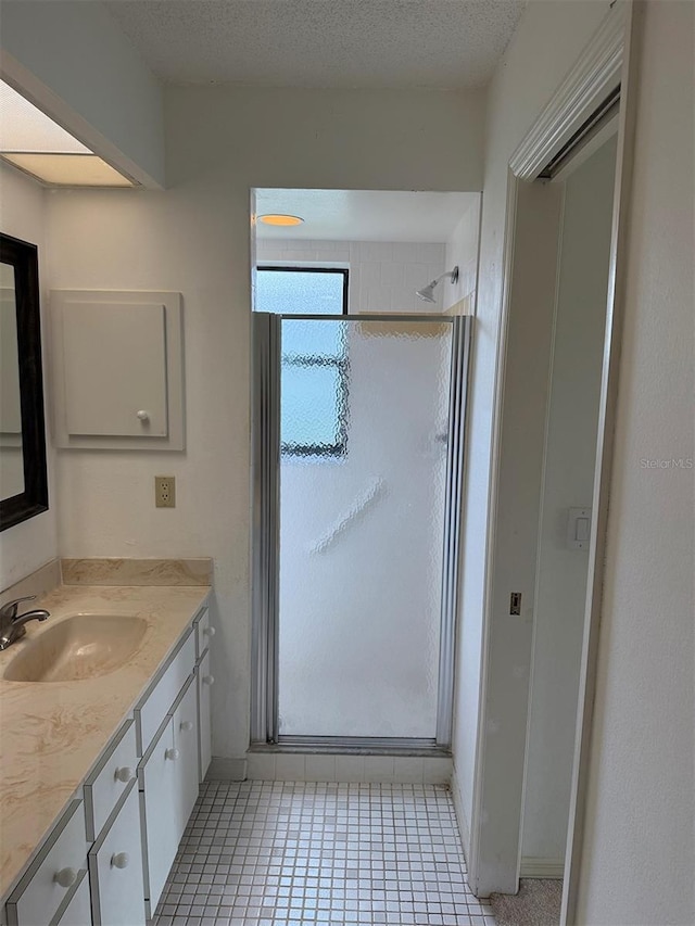 bathroom featuring a textured ceiling, tile patterned floors, walk in shower, and vanity