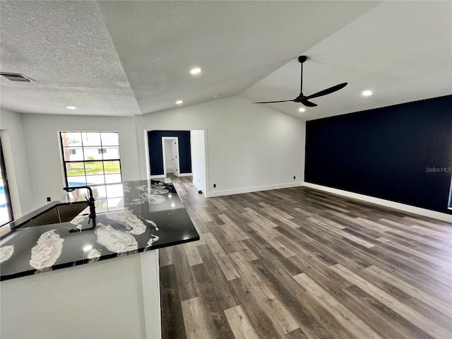 kitchen featuring lofted ceiling, a textured ceiling, dark stone countertops, ceiling fan, and hardwood / wood-style floors