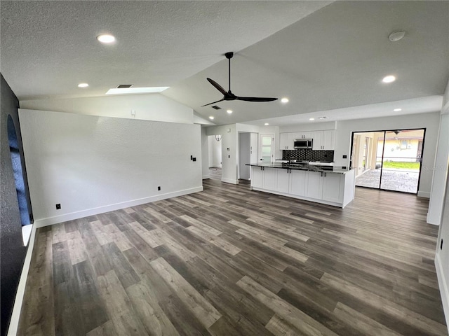 unfurnished living room featuring lofted ceiling, ceiling fan, dark hardwood / wood-style floors, and a textured ceiling