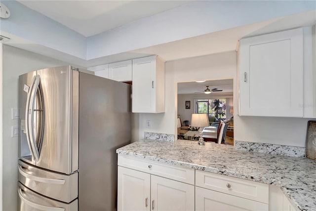 kitchen featuring ceiling fan, white cabinets, stainless steel fridge, and light stone counters