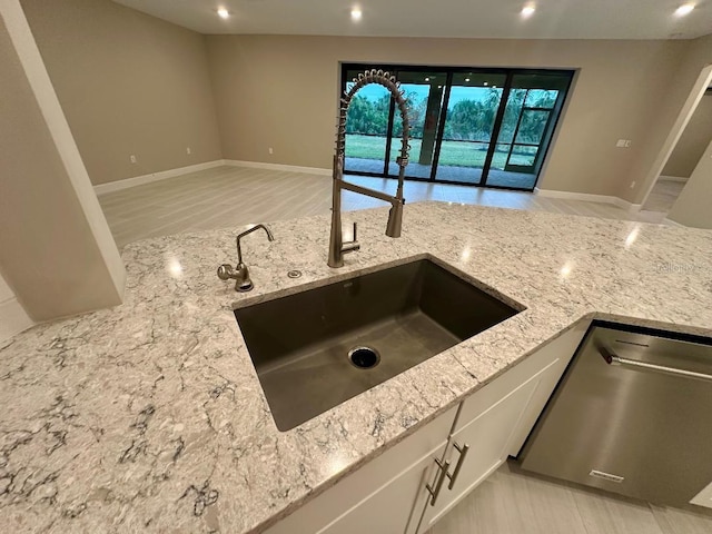 kitchen with stainless steel dishwasher, white cabinets, light stone counters, and sink