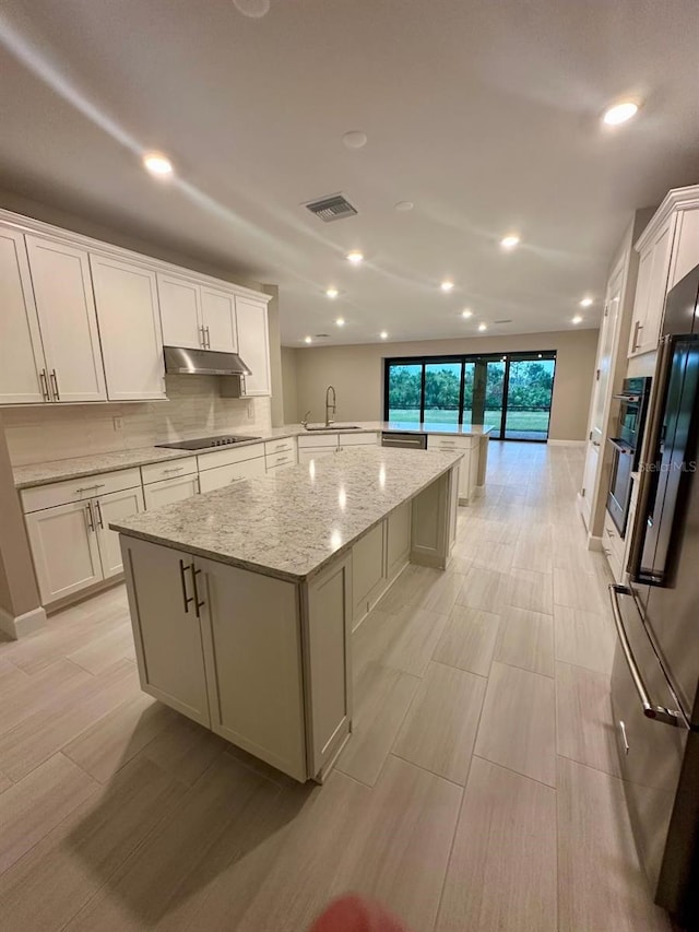 kitchen featuring tasteful backsplash, a spacious island, sink, white cabinetry, and light stone counters