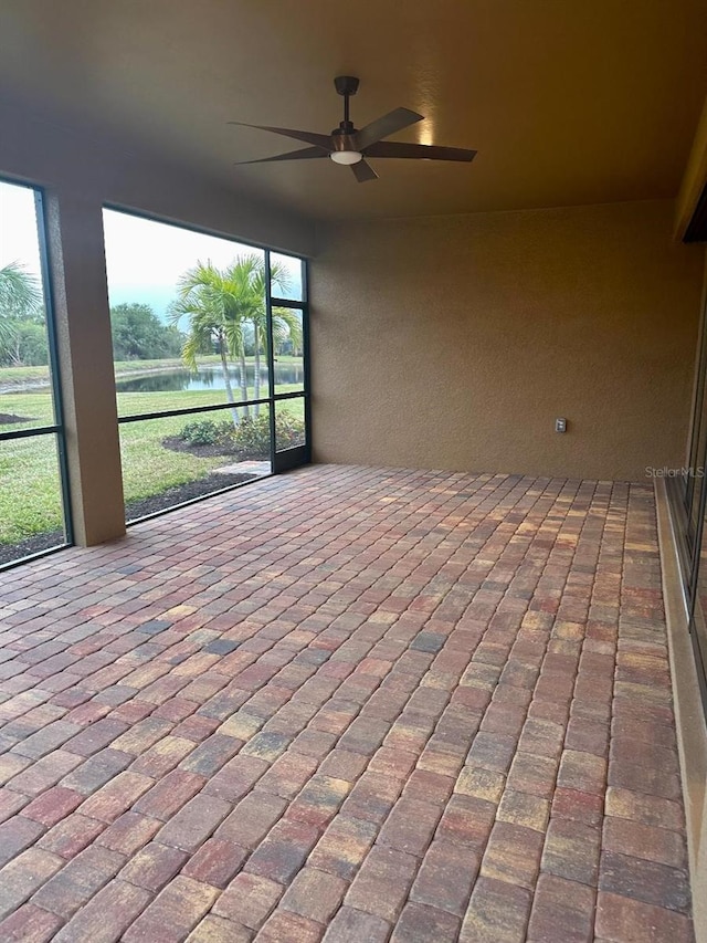 unfurnished sunroom featuring ceiling fan and a water view