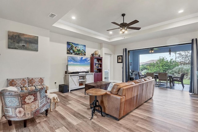 living room with ceiling fan, light hardwood / wood-style flooring, and a raised ceiling