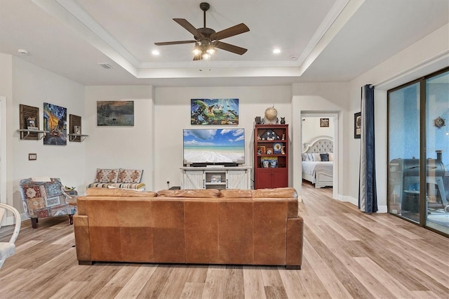 living room featuring light wood-type flooring, ceiling fan, and a raised ceiling