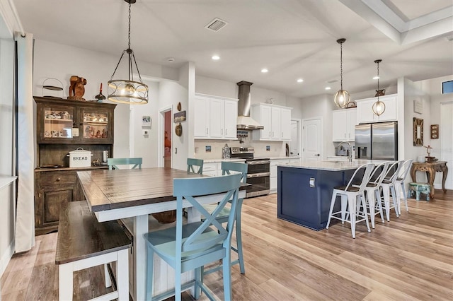 kitchen with appliances with stainless steel finishes, wall chimney range hood, a kitchen island, pendant lighting, and white cabinets