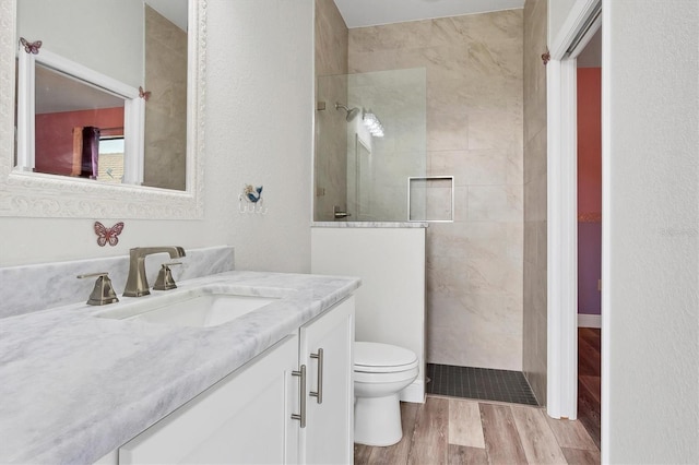 bathroom with vanity, toilet, hardwood / wood-style floors, and tiled shower