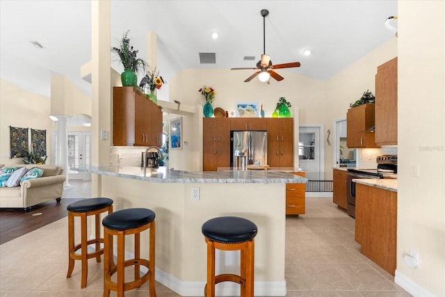 kitchen with appliances with stainless steel finishes, backsplash, kitchen peninsula, light tile patterned floors, and a breakfast bar area