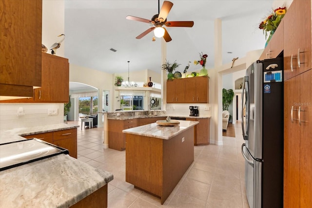 kitchen with kitchen peninsula, pendant lighting, stainless steel fridge, a center island, and high vaulted ceiling