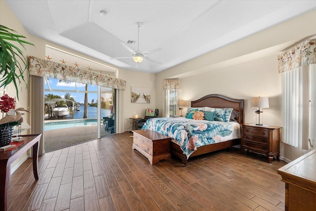 bedroom featuring hardwood / wood-style flooring, a raised ceiling, access to outside, a water view, and ceiling fan