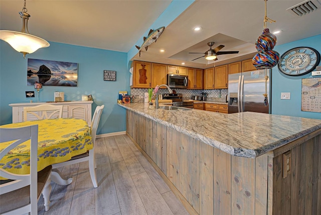 kitchen featuring pendant lighting, stainless steel appliances, a tray ceiling, light stone countertops, and kitchen peninsula