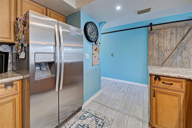 kitchen with a barn door, stainless steel fridge, light stone countertops, and decorative backsplash