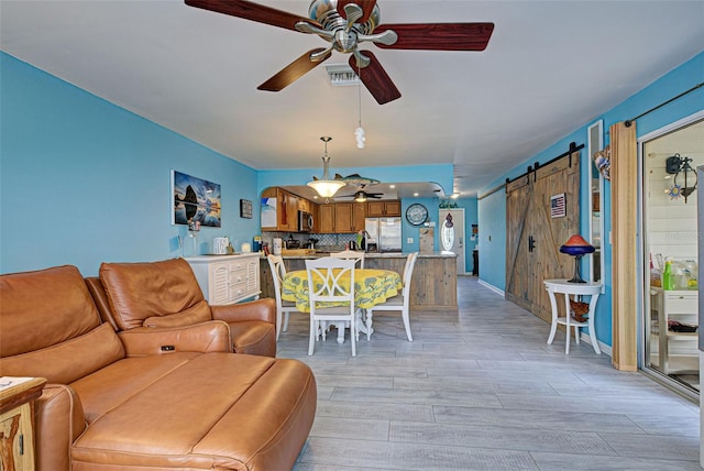 living room with ceiling fan, a barn door, and light hardwood / wood-style flooring