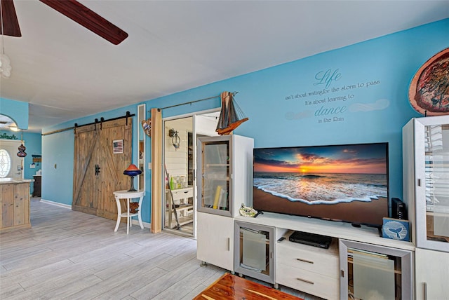 unfurnished living room with ceiling fan, a barn door, wine cooler, and light hardwood / wood-style floors