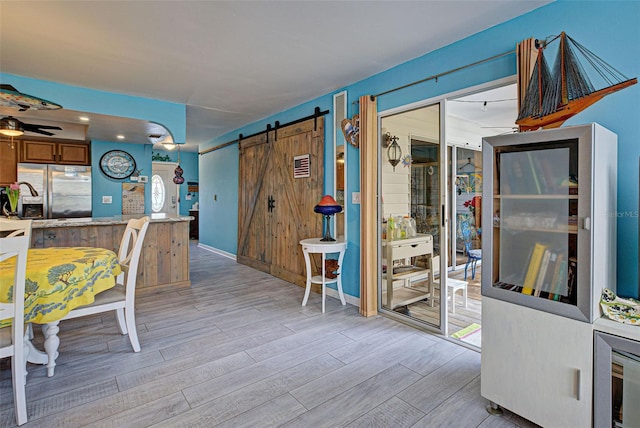 kitchen with ceiling fan, a barn door, light hardwood / wood-style floors, and stainless steel fridge with ice dispenser