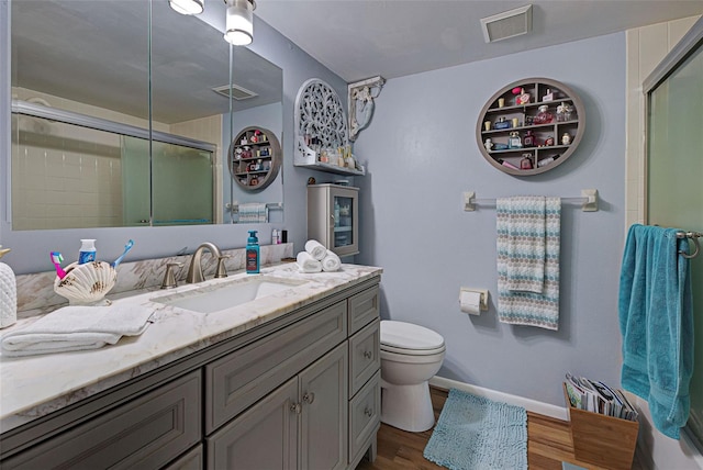 bathroom with toilet, wood-type flooring, vanity, and a shower with shower door