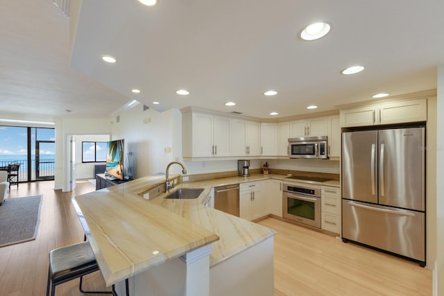 kitchen featuring kitchen peninsula, appliances with stainless steel finishes, a kitchen breakfast bar, white cabinets, and sink