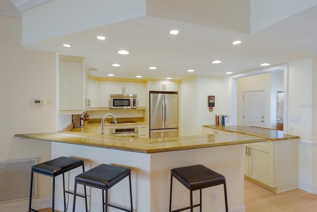 kitchen featuring a kitchen bar, light hardwood / wood-style floors, kitchen peninsula, and stainless steel appliances