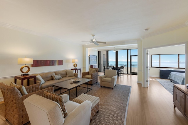 living room featuring ceiling fan, crown molding, a water view, and light wood-type flooring