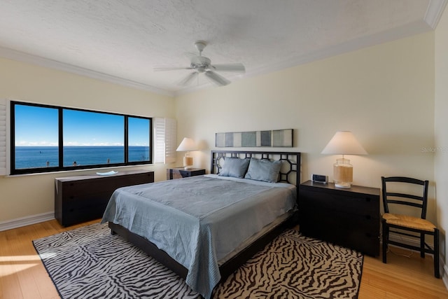 bedroom featuring light hardwood / wood-style floors, ceiling fan, a textured ceiling, crown molding, and a water view