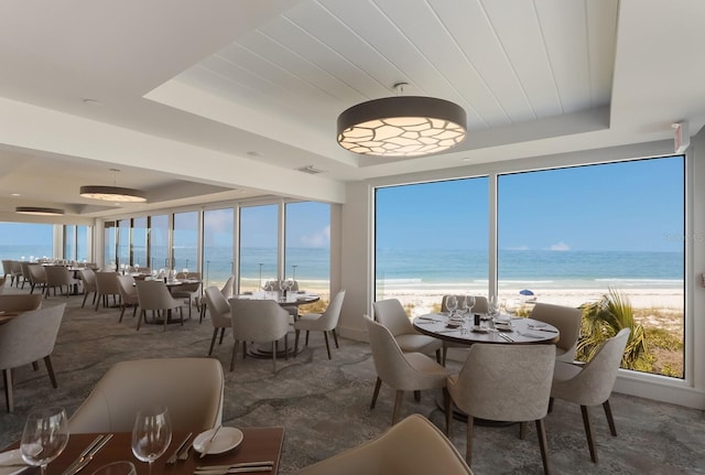 sunroom / solarium with a water view, a tray ceiling, and a view of the beach