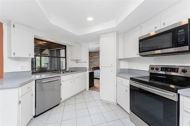 kitchen with light tile patterned flooring, sink, white cabinetry, a raised ceiling, and stainless steel appliances