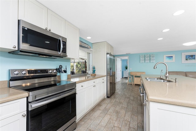 kitchen with appliances with stainless steel finishes, sink, white cabinets, and light wood-type flooring