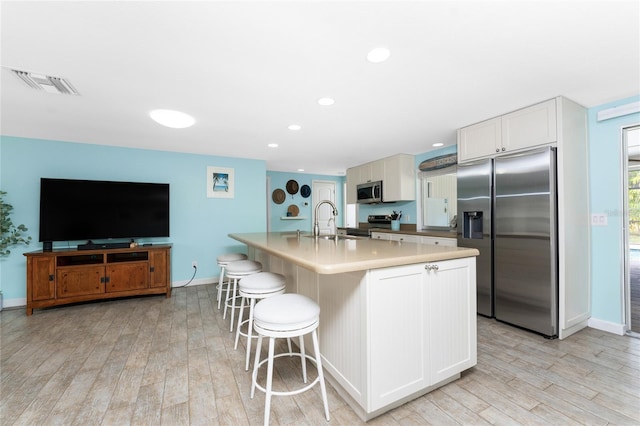 kitchen featuring sink, appliances with stainless steel finishes, white cabinetry, a kitchen breakfast bar, and a center island with sink