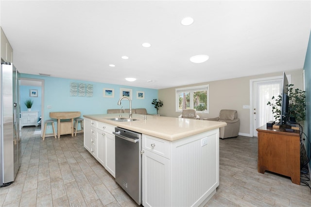 kitchen featuring white cabinetry, sink, light hardwood / wood-style floors, stainless steel appliances, and a center island with sink