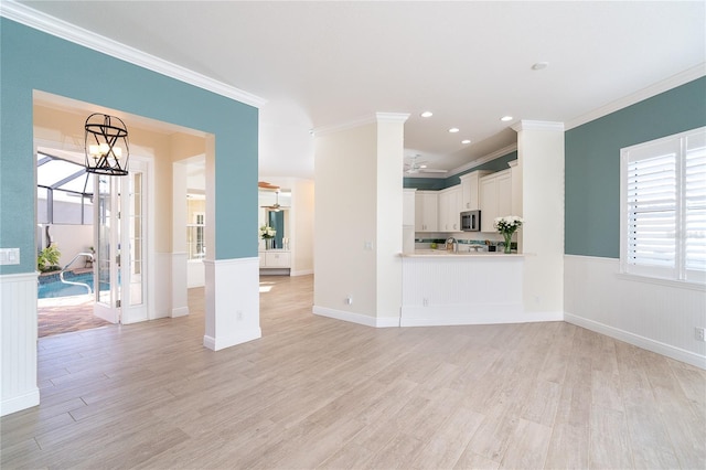 unfurnished living room featuring crown molding, ceiling fan with notable chandelier, and light wood-type flooring