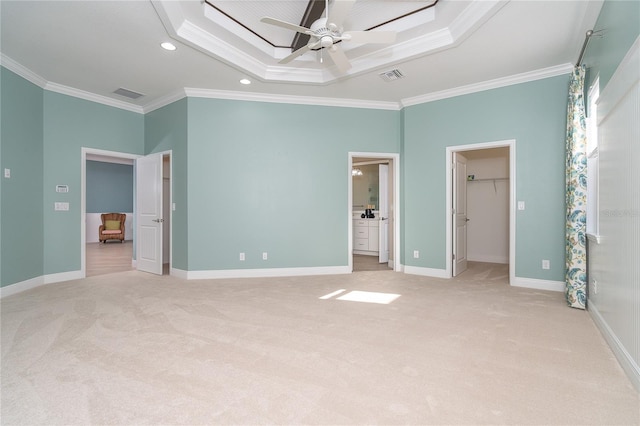 unfurnished bedroom with crown molding, light colored carpet, a tray ceiling, and a walk in closet