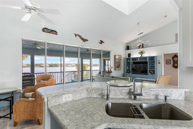 kitchen featuring vaulted ceiling, ceiling fan, sink, a water view, and light stone countertops