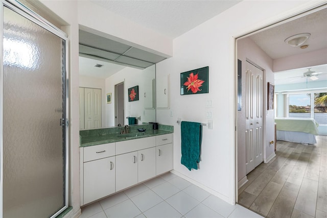 bathroom featuring ceiling fan, a textured ceiling, walk in shower, and vanity