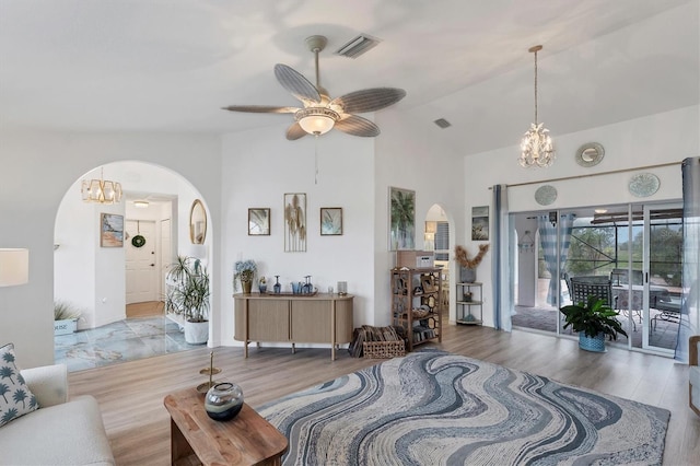 living room featuring ceiling fan with notable chandelier, vaulted ceiling, and light wood-type flooring