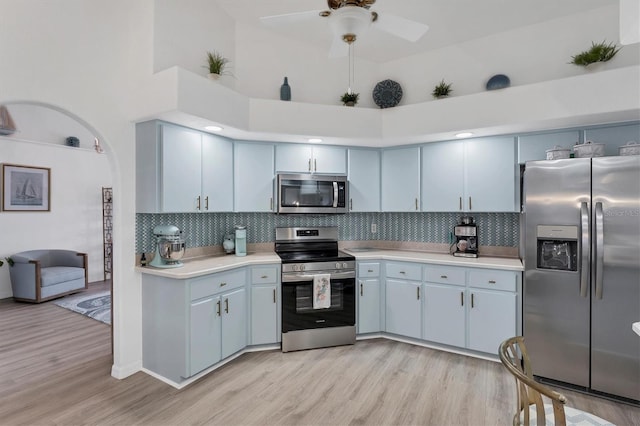 kitchen featuring appliances with stainless steel finishes, backsplash, a high ceiling, ceiling fan, and light hardwood / wood-style floors