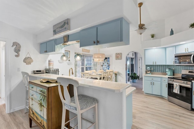 kitchen with blue cabinetry, appliances with stainless steel finishes, a kitchen breakfast bar, kitchen peninsula, and light wood-type flooring