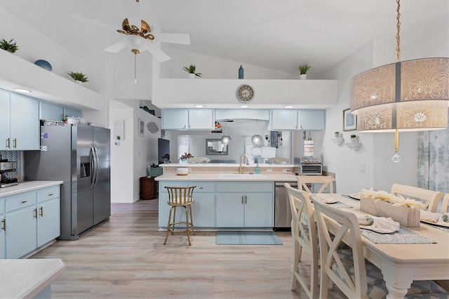 kitchen with sink, hanging light fixtures, stainless steel appliances, blue cabinetry, and light hardwood / wood-style flooring