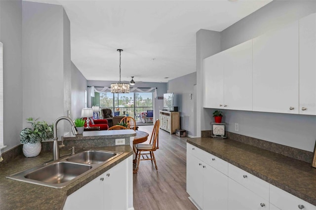 kitchen with hanging light fixtures, sink, light wood-type flooring, white cabinetry, and a notable chandelier