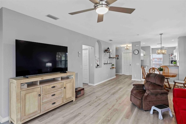 living room featuring ceiling fan with notable chandelier and light hardwood / wood-style flooring