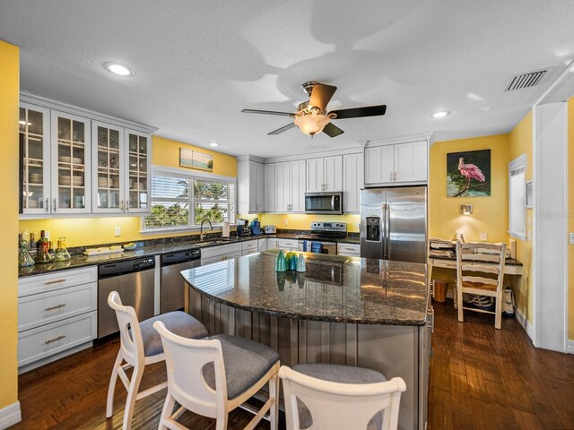 kitchen with appliances with stainless steel finishes, dark hardwood / wood-style floors, dark stone countertops, white cabinets, and a center island