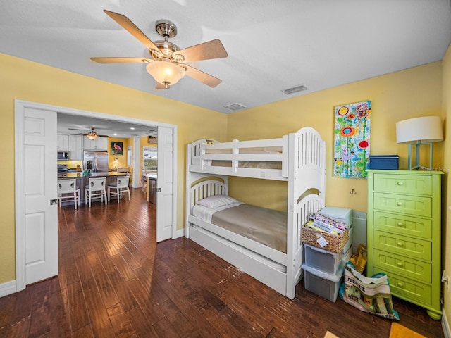 bedroom with dark wood-type flooring, ceiling fan, and stainless steel fridge with ice dispenser