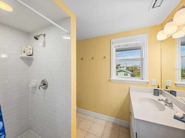 bathroom with tile patterned flooring, vanity, a textured ceiling, and tiled shower