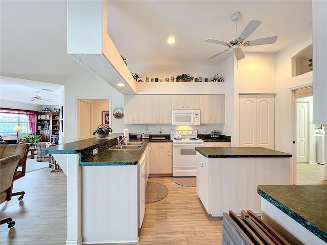 kitchen featuring white appliances, light wood finished floors, a peninsula, a sink, and dark countertops