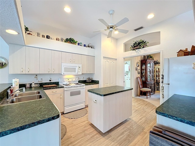 kitchen featuring visible vents, light wood-style flooring, a sink, a center island, and white appliances