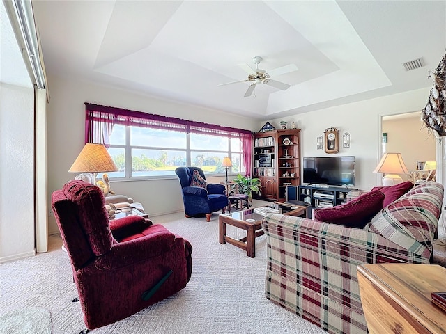 carpeted living room with visible vents, ceiling fan, baseboards, and a tray ceiling