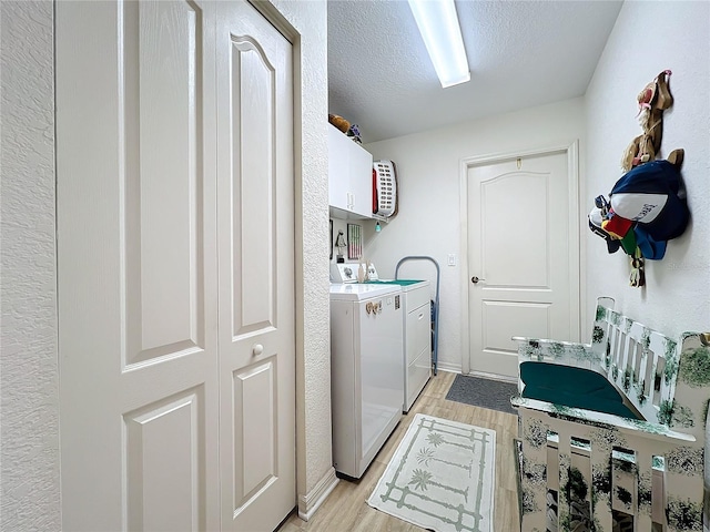 washroom with light wood-style flooring, cabinet space, separate washer and dryer, a textured ceiling, and a textured wall