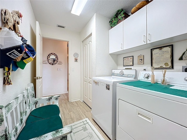 laundry area featuring visible vents, washing machine and clothes dryer, cabinet space, light wood-style floors, and a textured ceiling