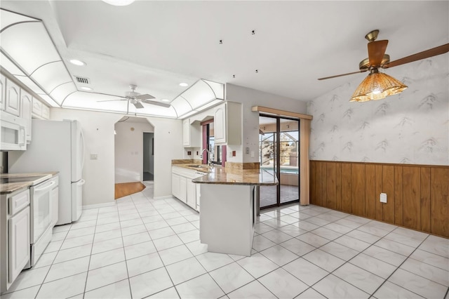 kitchen featuring a breakfast bar area, white cabinets, dark stone counters, ceiling fan, and white appliances